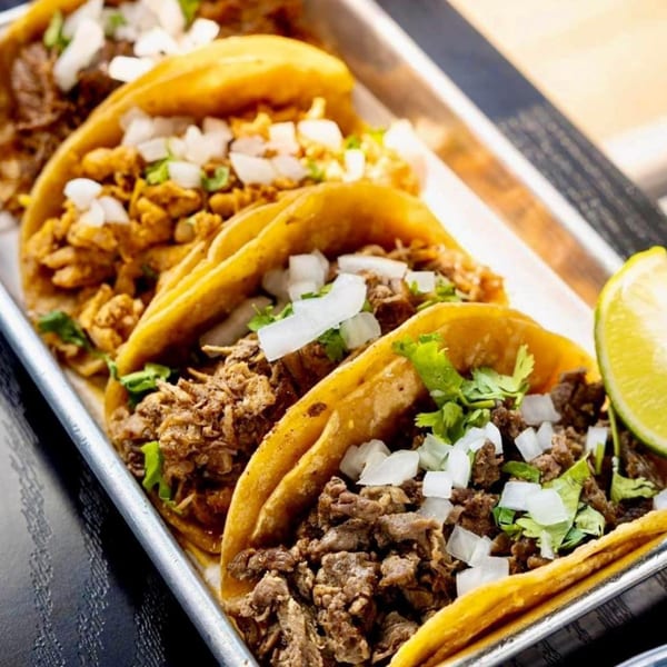 A metal tray holds five delicious Taco Depot tacos, garnished with onions, cilantro, and a lime wedge.