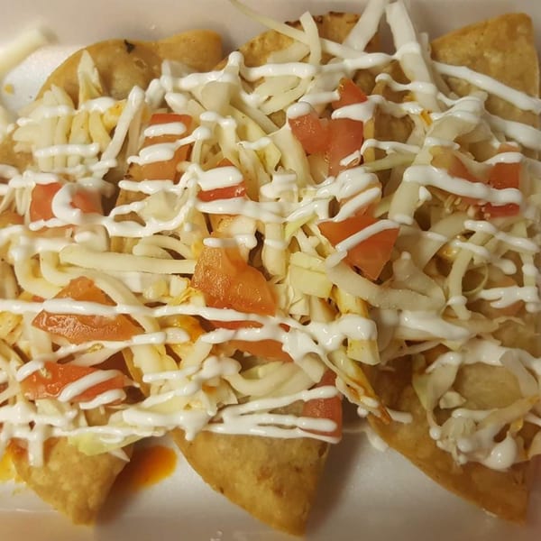 Three golden-fried tacos from Taco Depot, topped with shredded cheese, diced tomatoes, and a drizzle of sour cream.