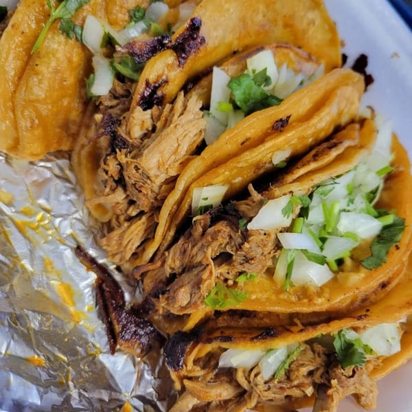 Close-up of several Taco Depot tacos with shredded meat, onions, and cilantro on foil.