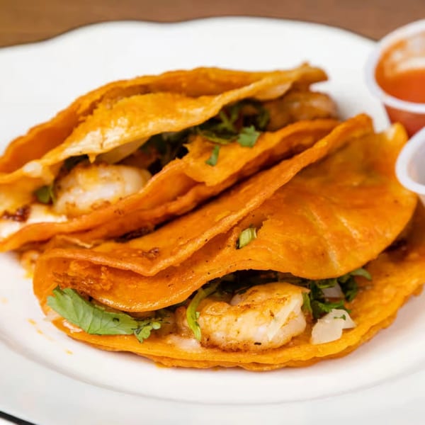 Three shrimp tacos with cilantro and onions on a white plate with two small sauce cups.