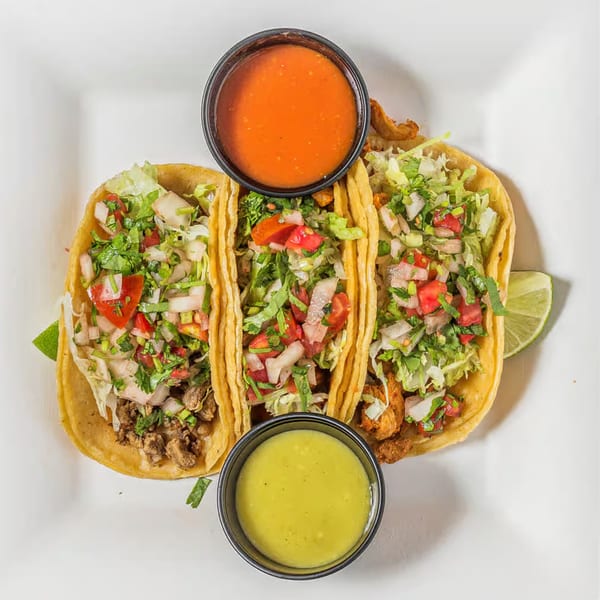 Three vibrant Taco Depot tacos with various fillings, fresh toppings, and two dipping sauces.